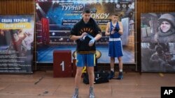 Young boxers prepare to fight during a boxing tournament in honor of Maksym Halinichev, in Romny, in Ukraine's Sumy region, Feb. 3, 2024. Images of Halinichev flank the central billboard.