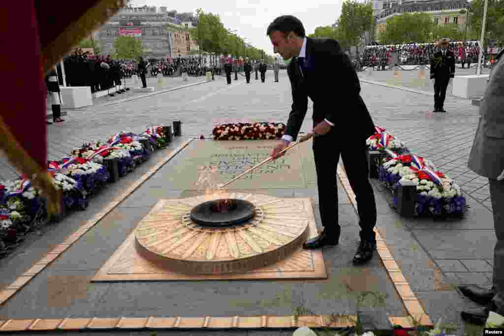 French President Emmanuel Macron lights the flame at the Tomb of the Unknown Soldier under the Arc de Triomphe during ceremonies commemorating the end of World War II anniversary (Victory Day), in Paris.