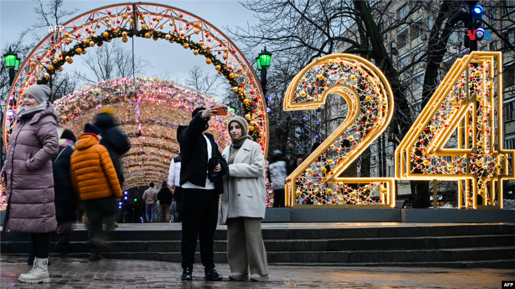  Desde Rusia: Los peatones posan frente a una decoración con números del Año Nuevo 2024 en el centro de Moscú el 31 de diciembre de 2023, en vísperas del Año Nuevo. &nbsp; 