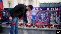 A man puts a candle at a makeshift memorial for Wagner mercenary group members killed in a plane crash last Wednesday, near the Kremlin in Moscow, Aug. 27, 2023. Listed among the dead was Yevgeniy Prigozhin, the group's leader (pictured to the left of the Wagner emblem).