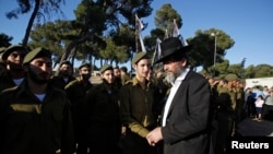 FILE - An ultra-Orthodox Jewish man walks past Israeli soldiers of the Netzah Yehuda Haredi infantry battalion during their swearing-in ceremony in Jerusalem, May 26, 2013. 