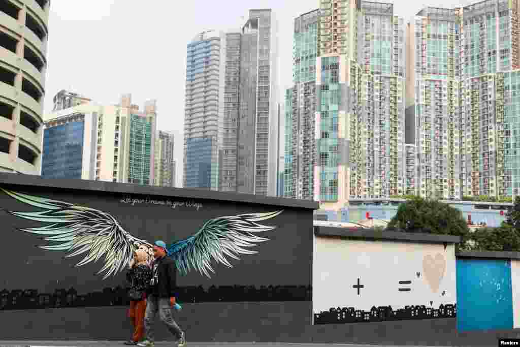 People walk beside a mural depicting wings with a background of office buildings and apartments in Jakarta, Indonesia.