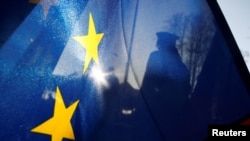 FILE - The silhouette of a border guard is seen through a European Union flag at a Czech crossing in Hradek nad Nisou, Feb. 26, 2019.