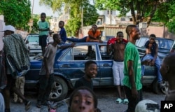 Para pemuda berada di dekat mobil yang berfungsi sebagai barikade jalanan yang ditempatkan di sana oleh warga untuk mencegah geng memasuki lingkungan mereka, di pusat kota Port-au-Prince, Haiti, 17 Mei 2024. (Foto: AP)