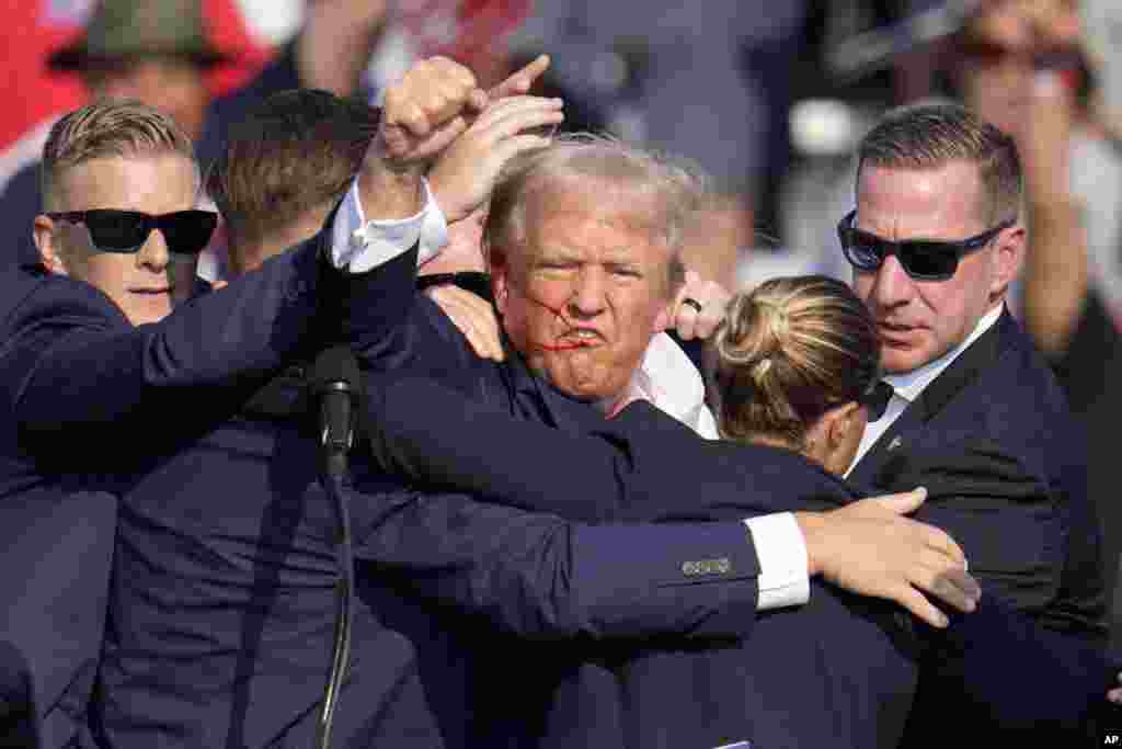 Donald Trump pumps his fist as he is helped off the stage.