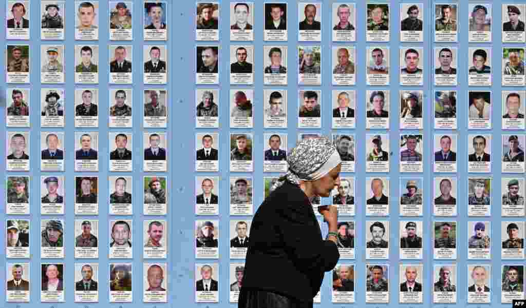 An elderly woman crosses herself as she walks past the Memory Wall of Fallen Defenders of Ukraine, in Kyiv.