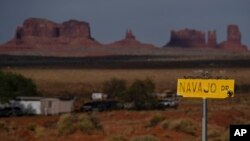 FILE - A sign marks Navajo Drive, with Sentinel Mesa, homes and other structures in Oljato-Monument Valley, Utah, on the Navajo Reservation, in the distance, on April 30, 2020.