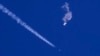 在美國南卡羅萊納州海岸被美軍擊落的中國間諜氣球殘餘物漂浮在空中，下方是美軍戰鬥機和它的尾跡（2023年2月4日）。