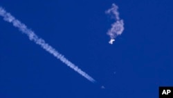 在美国南卡罗莱纳州海岸被美军击落的中国间谍气球残余物漂浮在空中，下方是美军战斗机和它的尾迹（2023年2月4日）。