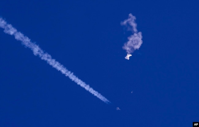 In this photo provided by Chad Fish, the remnants of a large balloon drift above the Atlantic Ocean, just off the coast of South Carolina, with a fighter jet and its contrail seen below it, Feb. 4, 2023. (Chad Fish via AP, File)