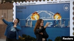 FILE - People take selfies in front of an enlarged replica of a stamp depicting Russia's Kerch bridge on fire, in central Kyiv, Ukraine Oct. 8, 2022. The bridge was built to connect Russian mainland to the Crimean peninsula which Moscow annexed from Ukraine in 2014.