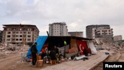 A family sits in an improvised shelter after their apartment building collapsed in an earthquake, in Antakya, southeastern Turkey, Feb. 21, 2023.