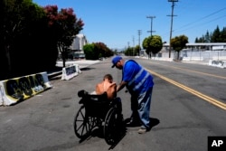 Ruben Rodriguez with Hope the Mission gives gives water to a homeless man in a wheelchair near the 405 Freeway in the Van Nuys section of Los Angeles, July 26, 2024.