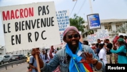 A demonstrator holds a sign that reads "Macron not welcomed in DRC" during a protest against the visit of the French President Emmanuel Macron in front of the French embassy in Kinshasa, Democratic Republic of Congo, March 1, 2023