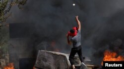 A Palestinian throws a stone during clashes with Israeli troops after Israeli settlers attack Umm Safa village near Ramallah, in the Israeli-occupied West Bank, June 24, 2023.