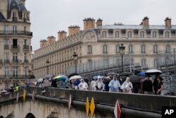 Pedestrians make their way across a sidewalk opened to foot traffic on the Pont Royal, or Royal Bridge, along grandstands used in the opening ceremonies, at the 2024 Summer Olympics, July 27, 2024, in Paris, France.