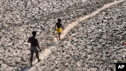 FILE - A man and a boy walk across a dried-up bed of river Yamuna in New Delhi, India, May 2, 2022. (AP Photo/Manish Swarup, File)