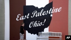 FILE - A skateboarder passes a sign in downtown East Palestine, Ohio, as the cleanup of portions of a Norfolk Southern freight train that derailed over a week ago continues, Feb. 15, 2023.