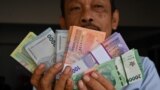 Seorang pria memperlihatkan uang kertas Rupiah baru yang akan diberikan kepada anggota keluarganya selama perayaan Idulfitri pada 28 Maret 2024. (Foto: AFP)