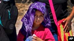 A young child and his mother, claiming to be from Guatemala, cools down with a wet bandana and a bottle of water as they wait to be picked up by U.S. Customs and Border Patrol, Aug. 29, 2023, in Organ Pipe Cactus National Monument near Lukeville, Ariz. 