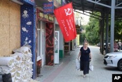 A woman walks past a shop decorated with a replica of a victory banner prior to local elections in Donetsk, the capital of Russian-controlled Donetsk region, eastern Ukraine, Sept. 7, 2023.