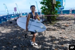 Yang Siqi, of China, smiles as she carries her surfboard on a training day ahead of the 2024 Summer Olympics surfing competition in Teahupo'o, Tahiti, July 25, 2024.