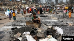FILE - A Rohingya refugee boy sits on a stack of burnt materials after a fire broke out and destroyed thousands of shelters at a refugee camp in Cox's Bazar, Bangladesh, March 24, 2021.