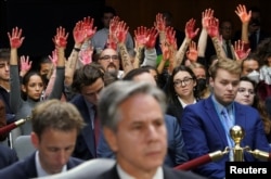 Anti-war protesters raise their "bloody" hands behind U.S. Secretary of State Antony Blinken during a Senate Appropriations Committee hearing on Capitol Hill in Washington, Oct. 31, 2023.