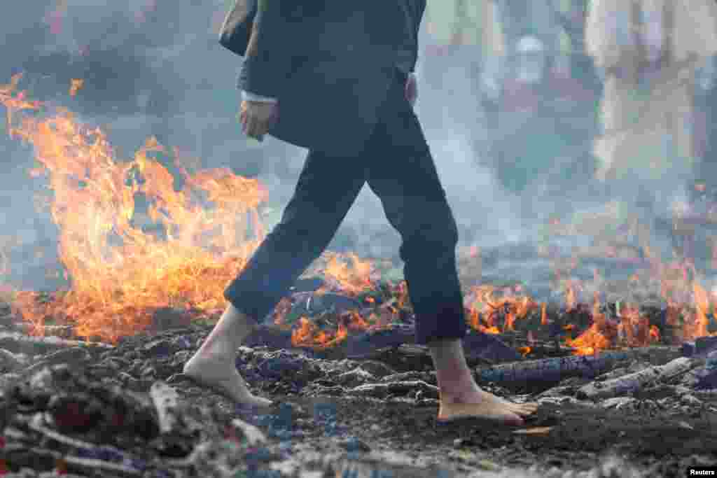 A man walks barefoot across hot embers, remains of a large bonfire of wood and Japanese cypress leaves, at the fire-walking festival at Mt.Takao in Tokyo, March 12, 2023. 