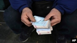 FILE - A street money exchanger counts Iranian banknotes at a commercial district in downtown Tehran, Dec. 23, 2022. Iran’s currency fell to a record low on March 24, 2024, plunging to 613,500 to the dollar, as its people celebrated the Persian New Year. 