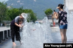FILE - A woman cools off with her grandson in a public fountain in Seoul, South Korea, Wednesday, June 19, 2024. (AP Photo/Ahn Young-joon)