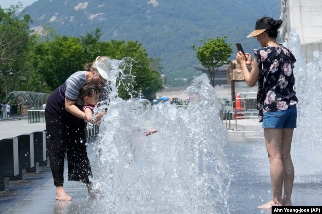 FILE - A woman cools off with her grandson in a public fountain in Seoul, South Korea, Wednesday, June 19, 2024. (AP Photo/Ahn Young-joon)