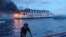 In this handout photo provided by the Philippine Coast Guard, a man pushes a boat beside a burning Philippine ferry off Panglao, Bohol province, central Philippines, June 18, 2023. 