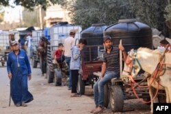 Palestinians gather next to donkey-drawn carts loaded with water tanks for sale, as drinking water and fuel become increasingly scarce, in Khan Yunis in the southern Gaza Strip, Oct. 30, 2023