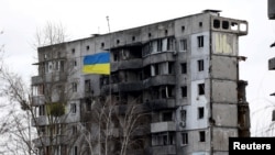 A Ukrainian national flag flies in front of a destroyed residential building amid Russia's invasion of Ukraine, in Borodianka, Kyiv region, Feb. 18, 2023. 