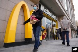 Seorang pria membawa makanan McDonald's miliknya saat orang-orang melakukan pemesanan di mesin di restoran McDonald's yang baru dibuka pada Minggu, 24 Desember 2023. (Foto: AP)