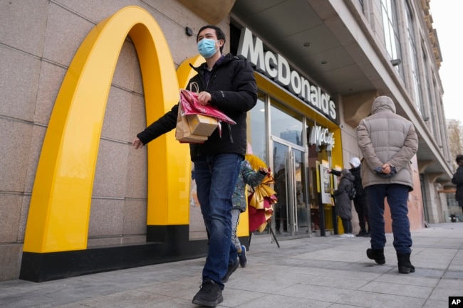 Seorang pria membawa makanan McDonald's miliknya saat orang-orang melakukan pemesanan di mesin di restoran McDonald's yang baru dibuka pada Minggu, 24 Desember 2023. (Foto: AP)