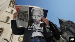 FILE - A demonstrator, holding a poster protesting the possible extradition to the U.S. of WikiLeaks founder Julian Assange, reads a newspaper outside the High Court in London, May 20, 2024.