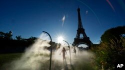 A spectator walks through mist sprayers on her way to Eiffel Tower Stadium to watch a beach volleyball match at the 2024 Summer Olympics, in Paris, France, July 28, 2024.