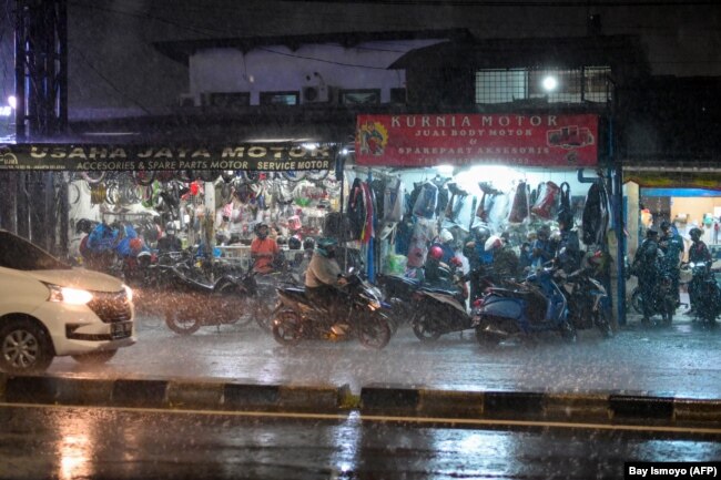 Pengendara sepeda motor berhenti di depan pertokoan pinggir jalan untuk berteduh dari hujan saat hujan deras di Jakarta pada 19 Januari 2022. (Foto: BAY ISMOYO/AFP)