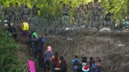 Texas state police finish placing barbed-wire as migrants walk up the bank of the Rio Grande river, seen from Matamoros, Mexico, May 10, 2023. 