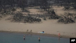 FILE - People play with a ball in front of a burnt forest at a beach of Glystra, on the Aegean Sea island of Rhodes, southeastern Greece, on July 27, 2023.