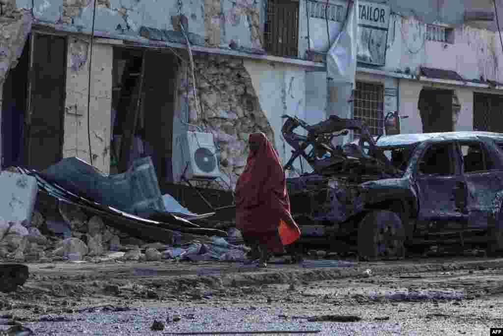 Seorang wanita Somalia berjalan melewati puing-puing dan kehancuran di sebuah kafe tempat para penggemar sepak bola menonton final Euro 2024 pasca ledakan bom mobil yang menewaskan lima orang, di ibukota Mogadishu. (AFP)