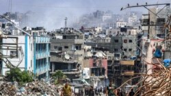 People walk past a mound of trash and destroyed buildings as behind smoke rises during Israeli bombardment in Jabalia in the northern Gaza Strip, May 14, 2024.