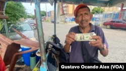 Un vendedor ambulante de golosinas y cigarros muestra un billete de un dólar estadounidense en Maracaibo, Venezuela.