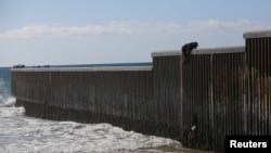 A migrant climbs the border fence to cross into the US to request asylum, at Playas de Tijuana, in Tijuana, Mexico, Oct. 2, 2023. 