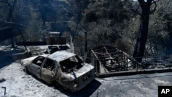 A charred vehicle and homes lie in ruins after a wildfire swept through the suburb of Nea Penteli in Athens, Aug. 13, 2024.