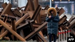 A woman looks at her phone as she walks past anti-tank constructions in the center of Kyiv on March 1, 2023. 
