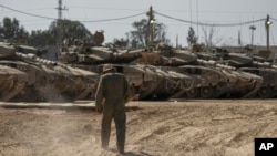 Israeli soldiers work on tanks at a staging ground near the border with the Gaza Strip, in southern Israel, April 11, 2024.