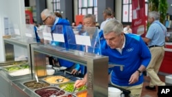 O Presidente do COI, Thomas Bach, prova comida de um bar de saladas enquanto visita a Aldeia Olímpica antes dos Jogos Olímpicos em Paris, França. 